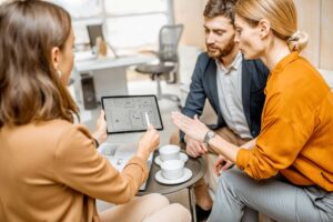A real estate agent and couple reviewing property documents at a kitchen table.