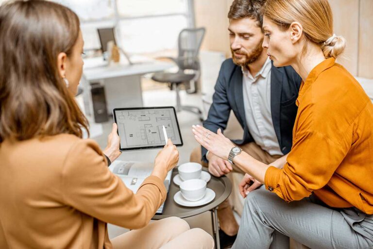 A real estate agent and couple reviewing property documents at a kitchen table.